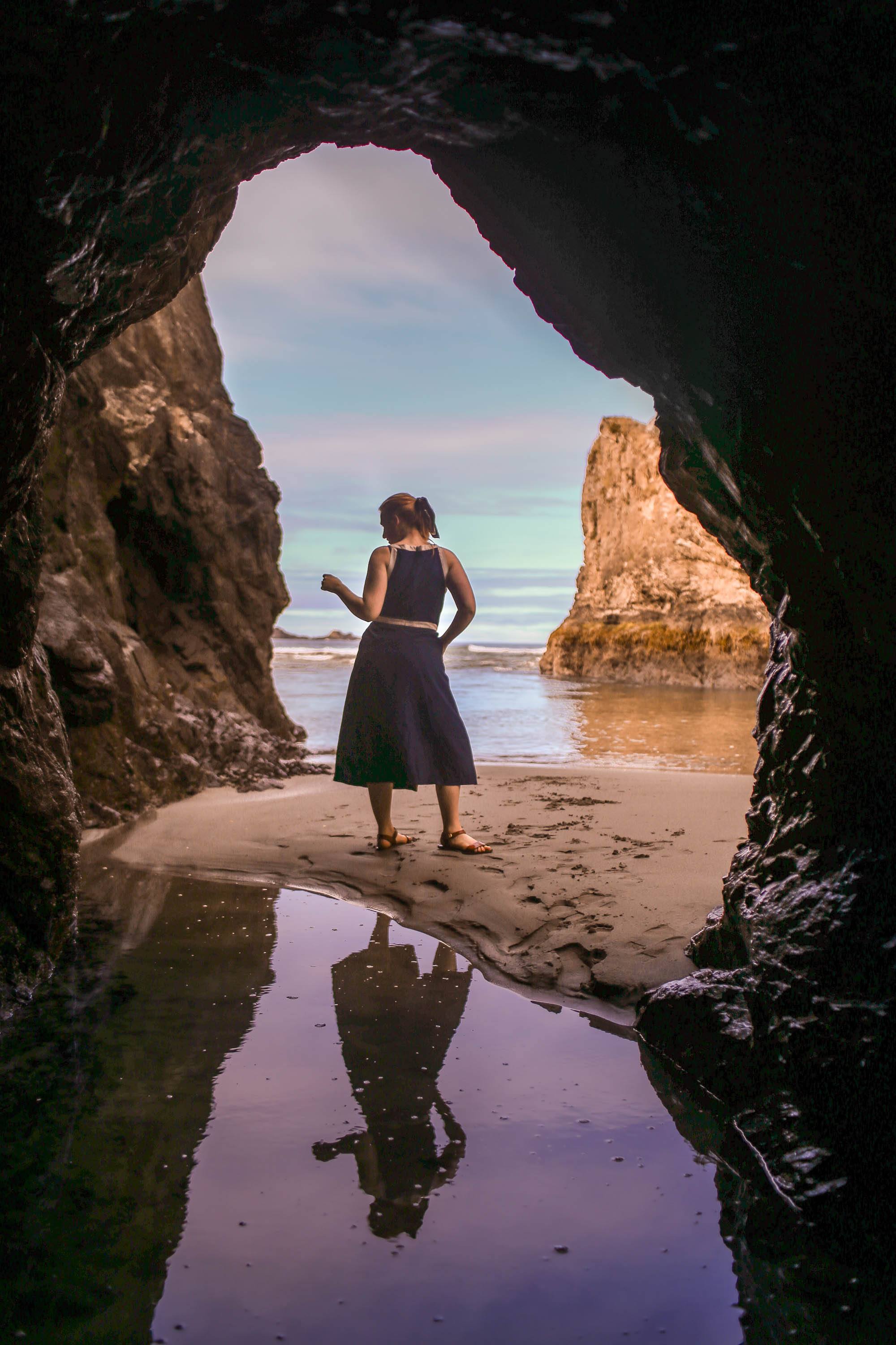 Woman in blue dress standing on beach through cave opening