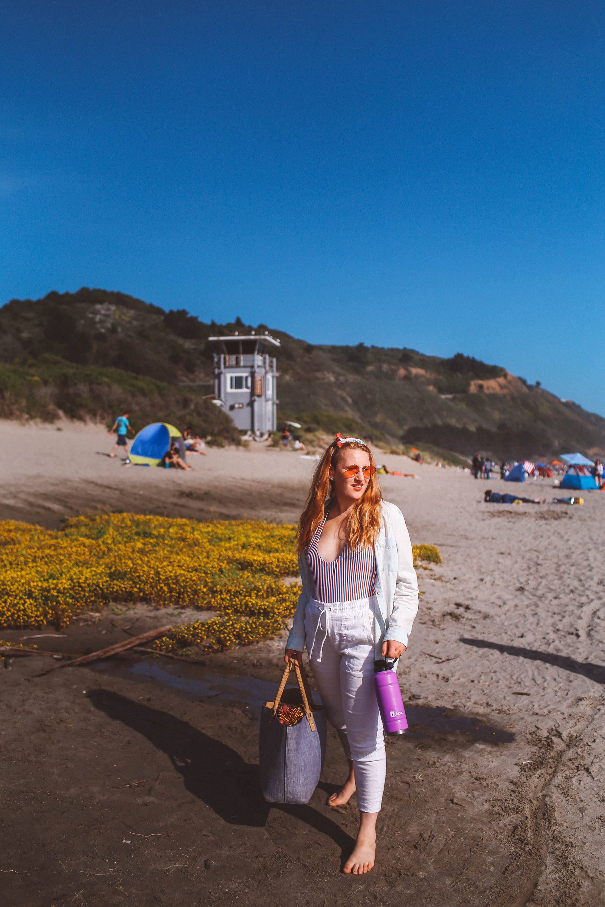Woman wearing rose colored sunglasses, white pants and a striped swimsuit at Stinson Beach