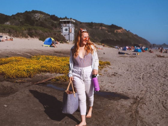 Woman wearing rose colored sunglasses, white pants and a striped swimsuit at Stinson Beach