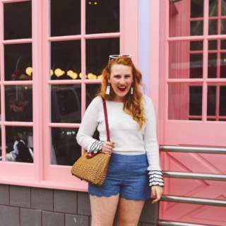 Woman wearing white rimmed sunglasses a white sweater and scallop shorts