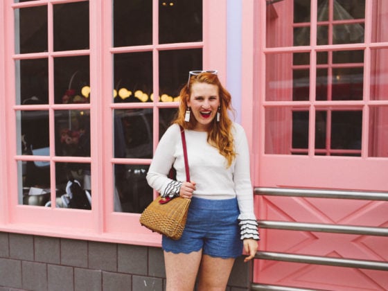 Woman wearing white rimmed sunglasses a white sweater and scallop shorts