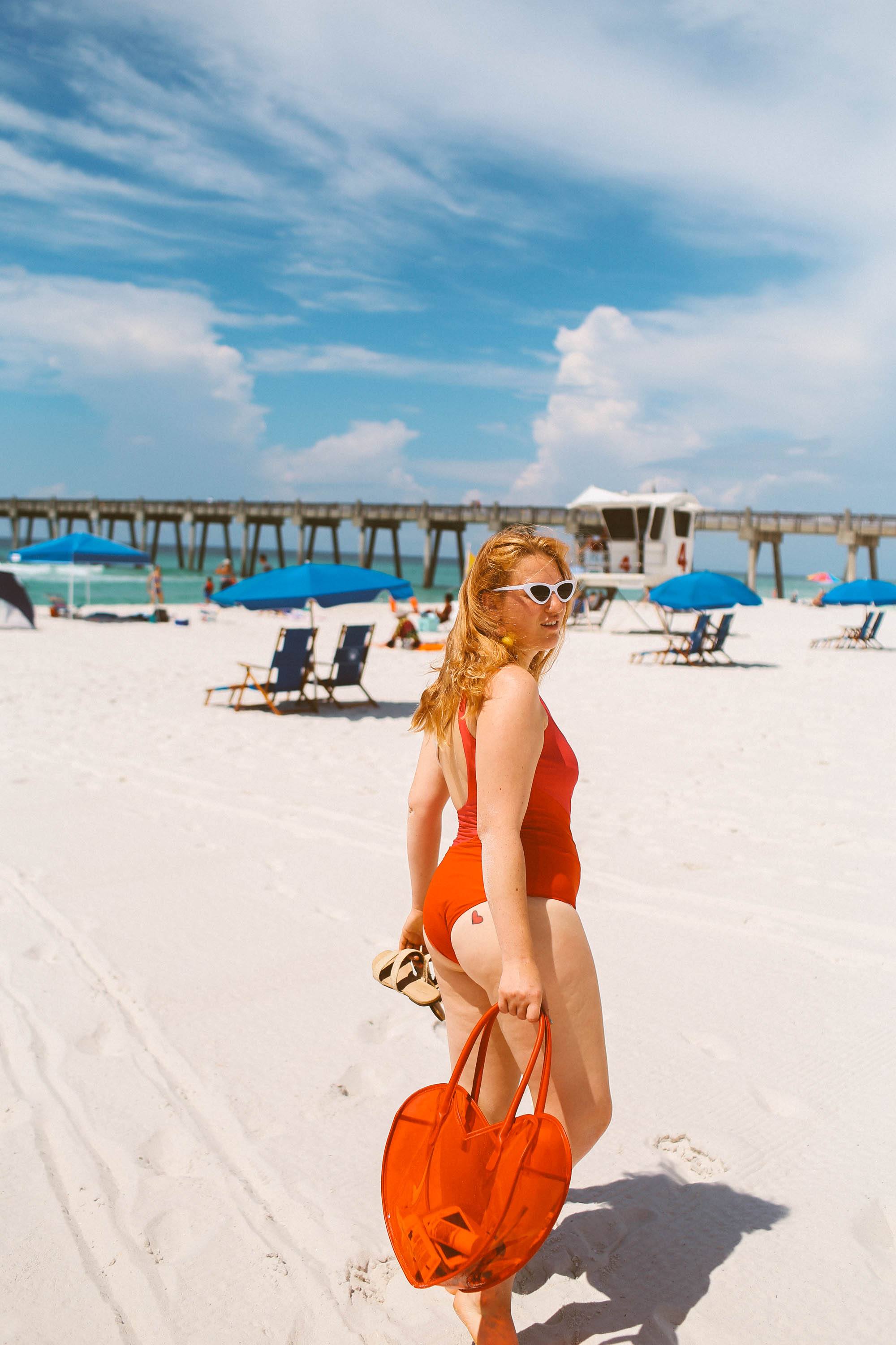 Woman in orange and white swimsuit holding a heart shaped bag at the beach