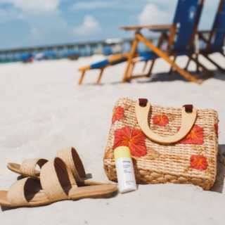 sandals, sunscreen and a floral straw purse on the sand