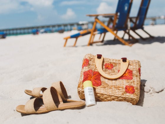 sandals, sunscreen and a floral straw purse on the sand