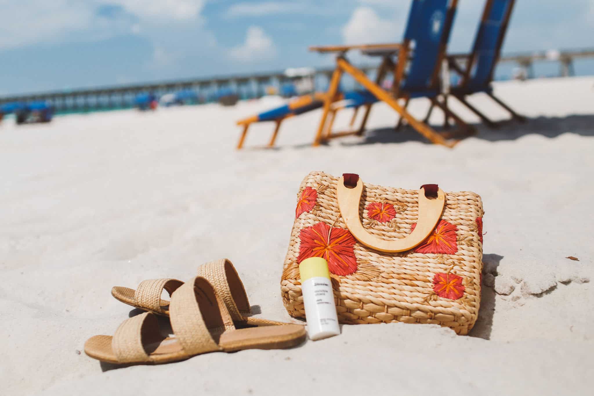 sandals, sunscreen and a floral straw purse on the sand