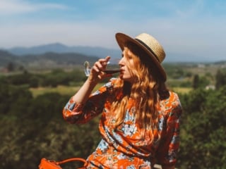 Woman in red floral dress and straw hat drinking wine on a ledge at a Napa Valley Winery