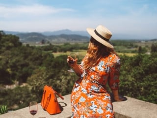 Woman in red floral dress and straw hat drinking wine on a ledge at a Napa Valley Winery