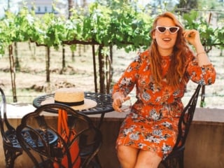 Woman in a red floral dress and sunglasses sitting at a table at Whitehall Lane Vineyard