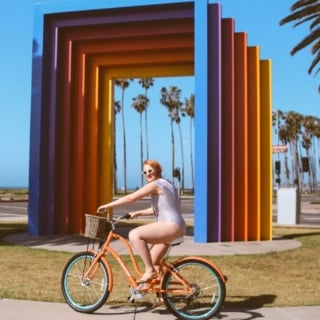 Woman in black and white striped front tie swimsuit riding a bike at the chromatic gate in Santa Barbara