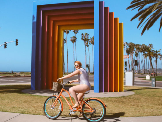 Woman in black and white striped front tie swimsuit riding a bike at the chromatic gate in Santa Barbara