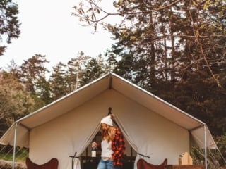 Woman standing on wood porch with wine in front of a tent