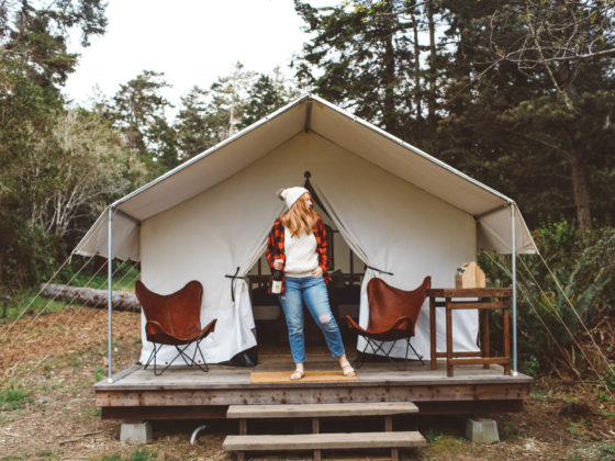 Woman standing on wood porch with wine in front of a tent