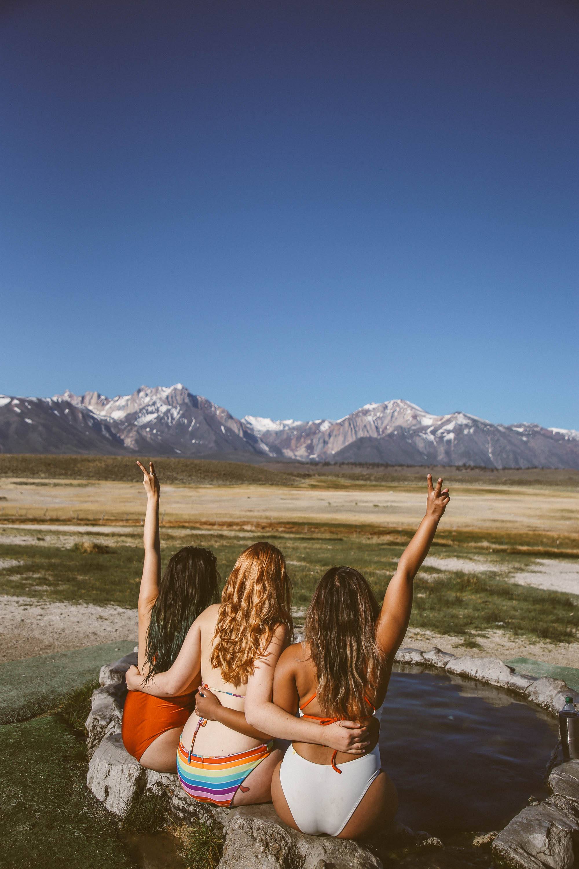 three woman sitting on the edge of a hot spring in the mountains