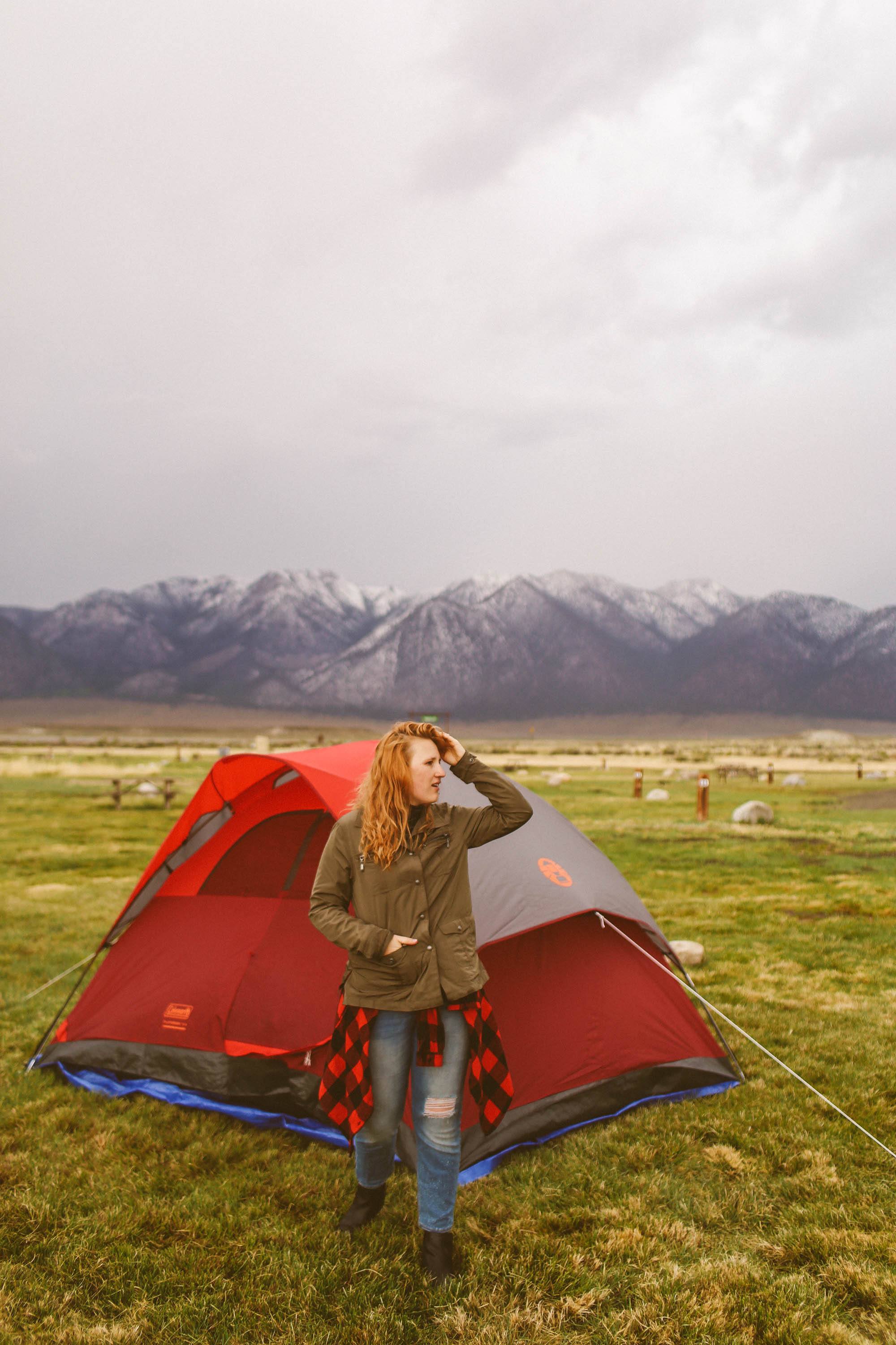 Woman standing in front of tent with mountains in the background