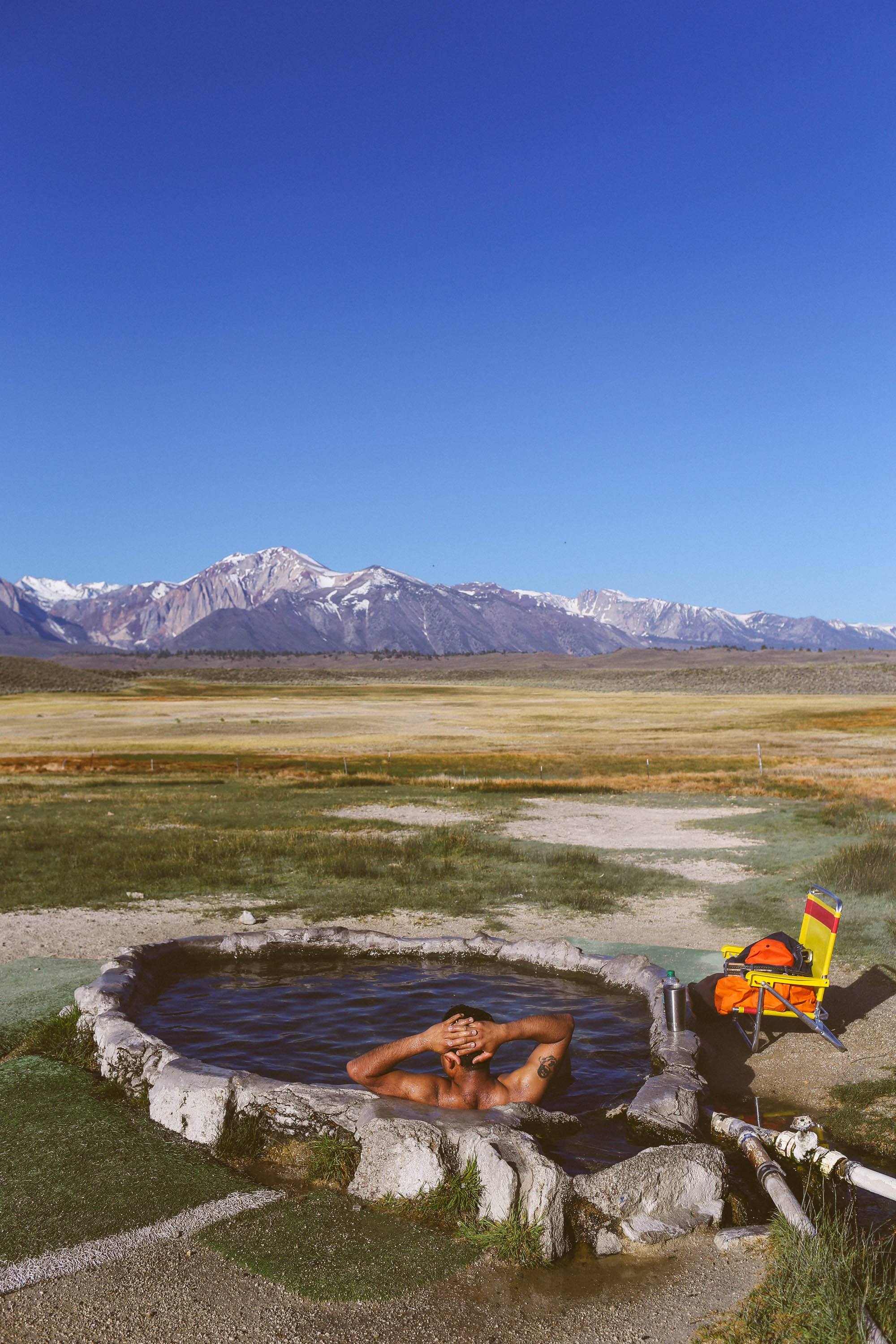 man in hot spring looking out over the plains, mountains in the background