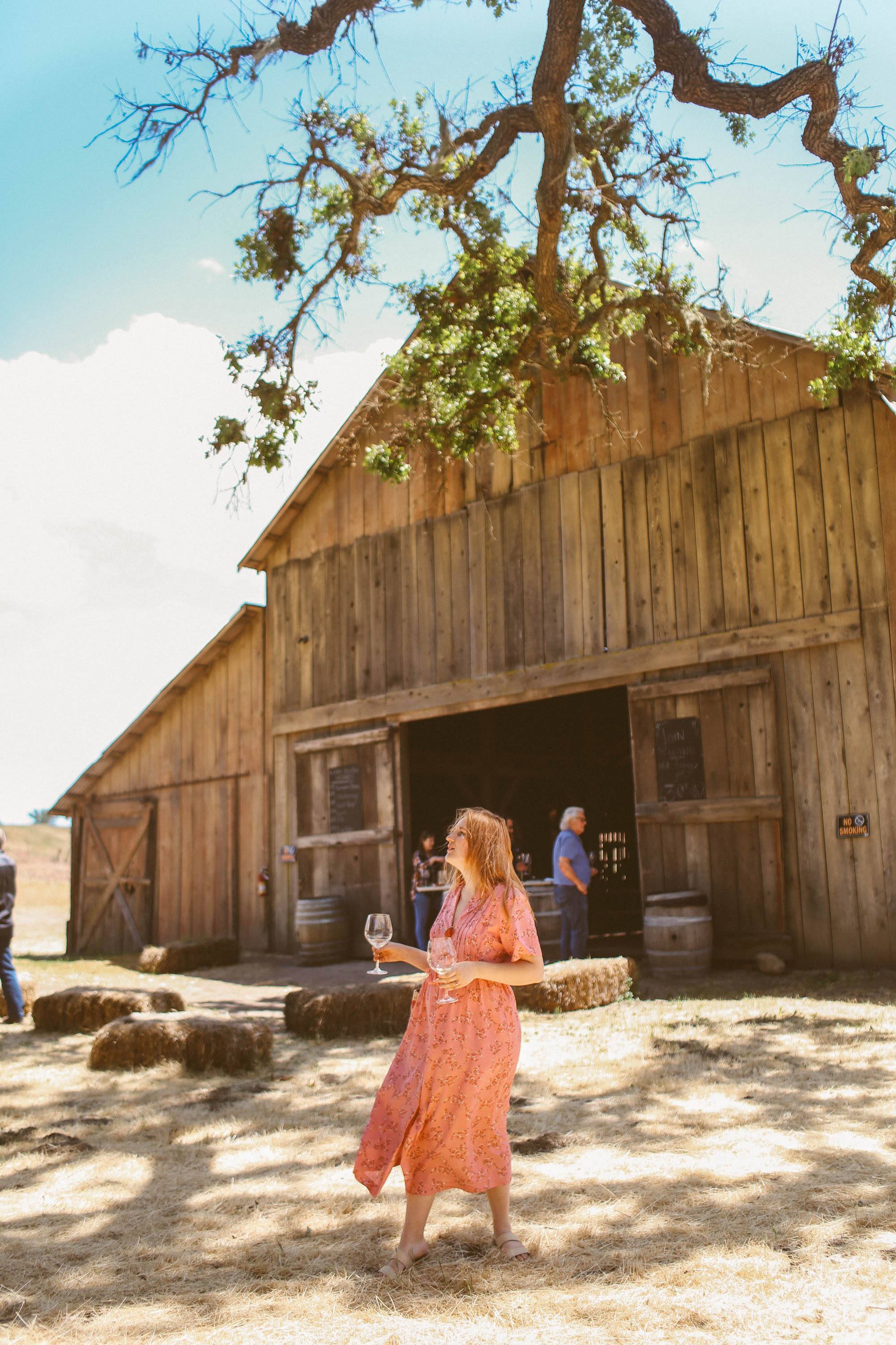 Woman holdin wine glasses in front of barn at Gainey Vineyard