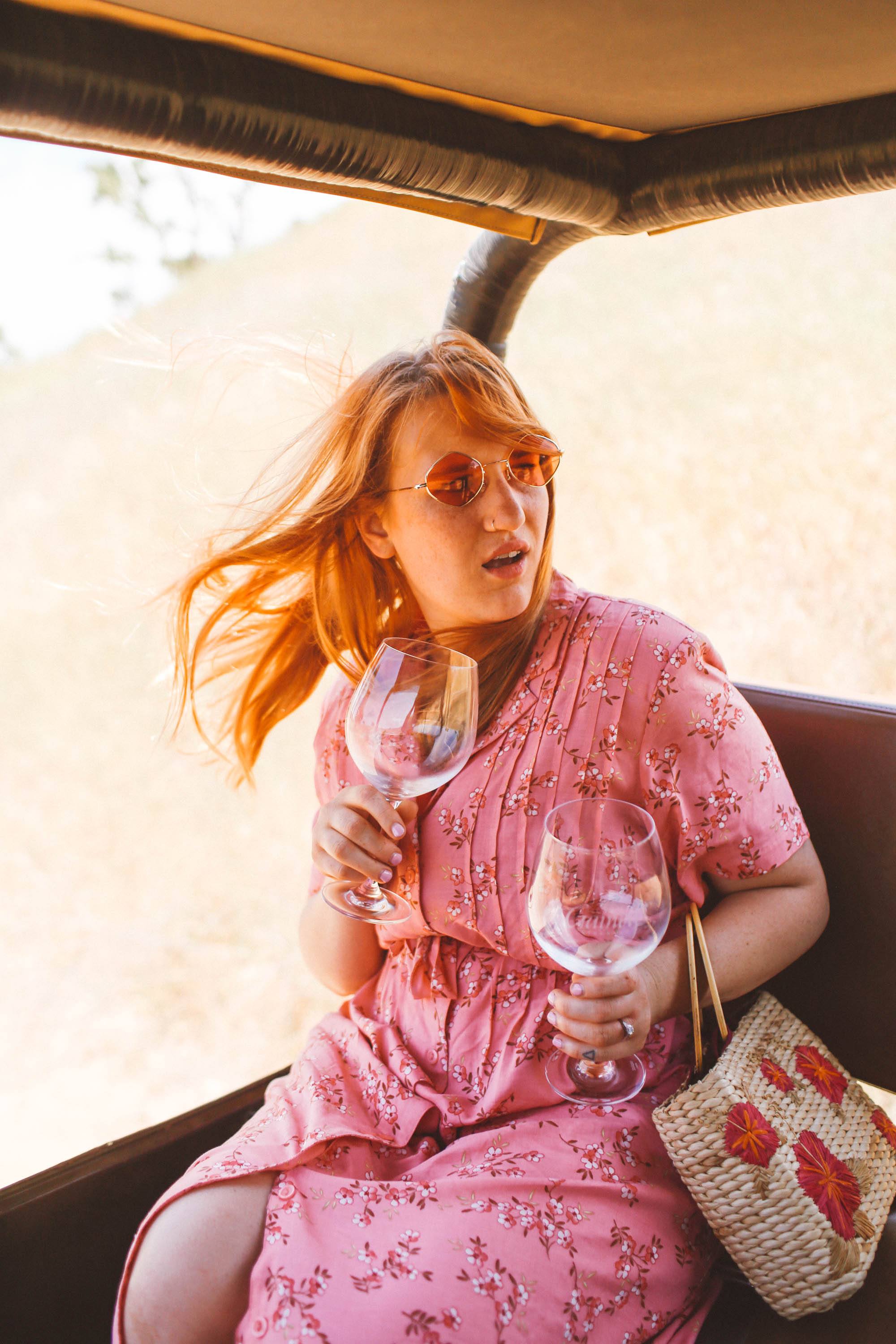 Woman in vintage pink dress holding wine glasses on jeep ride