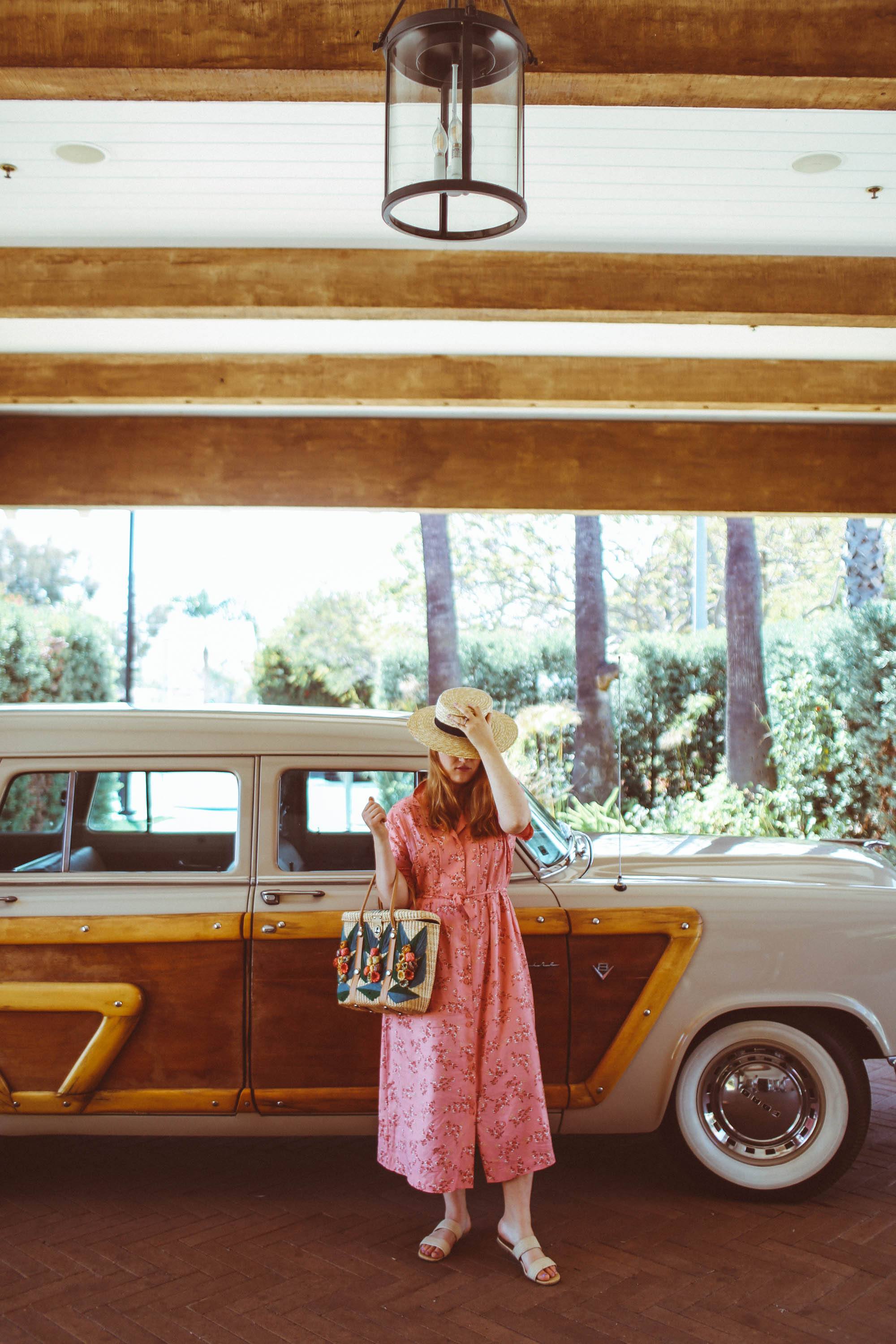 Woman in straw hat and pink vintage dress in front of classic car