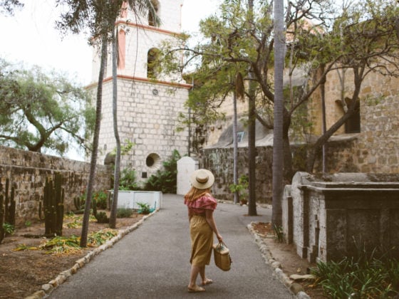 Woman wearing hat, red gingham top and a paper bag skirt at the Santa barbara mission