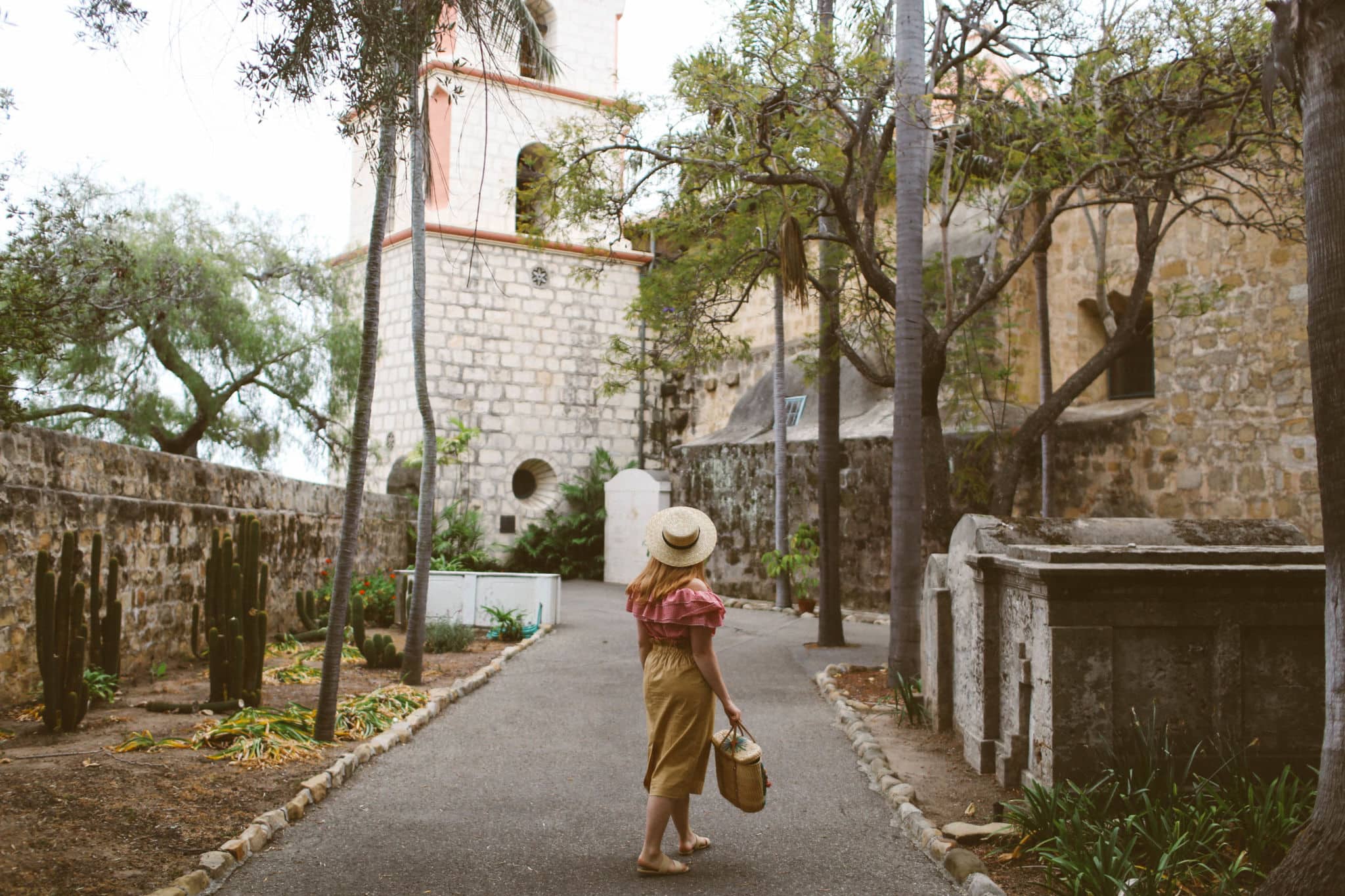 Woman wearing hat, red gingham top and a paper bag skirt at the Santa barbara mission