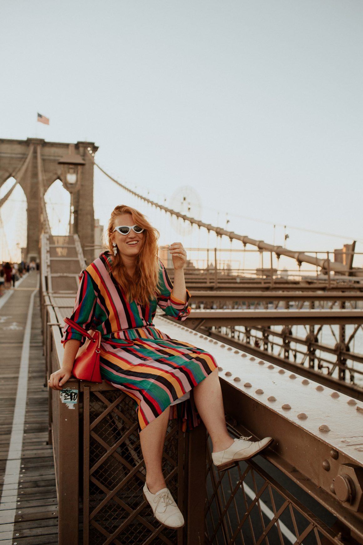 Woman in a rainbow Outfit sitting on the Brooklyn Bridge.