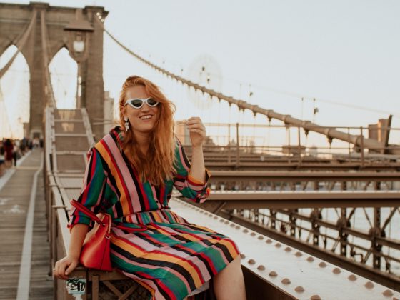 Woman in a rainbow Outfit sitting on the Brooklyn Bridge.