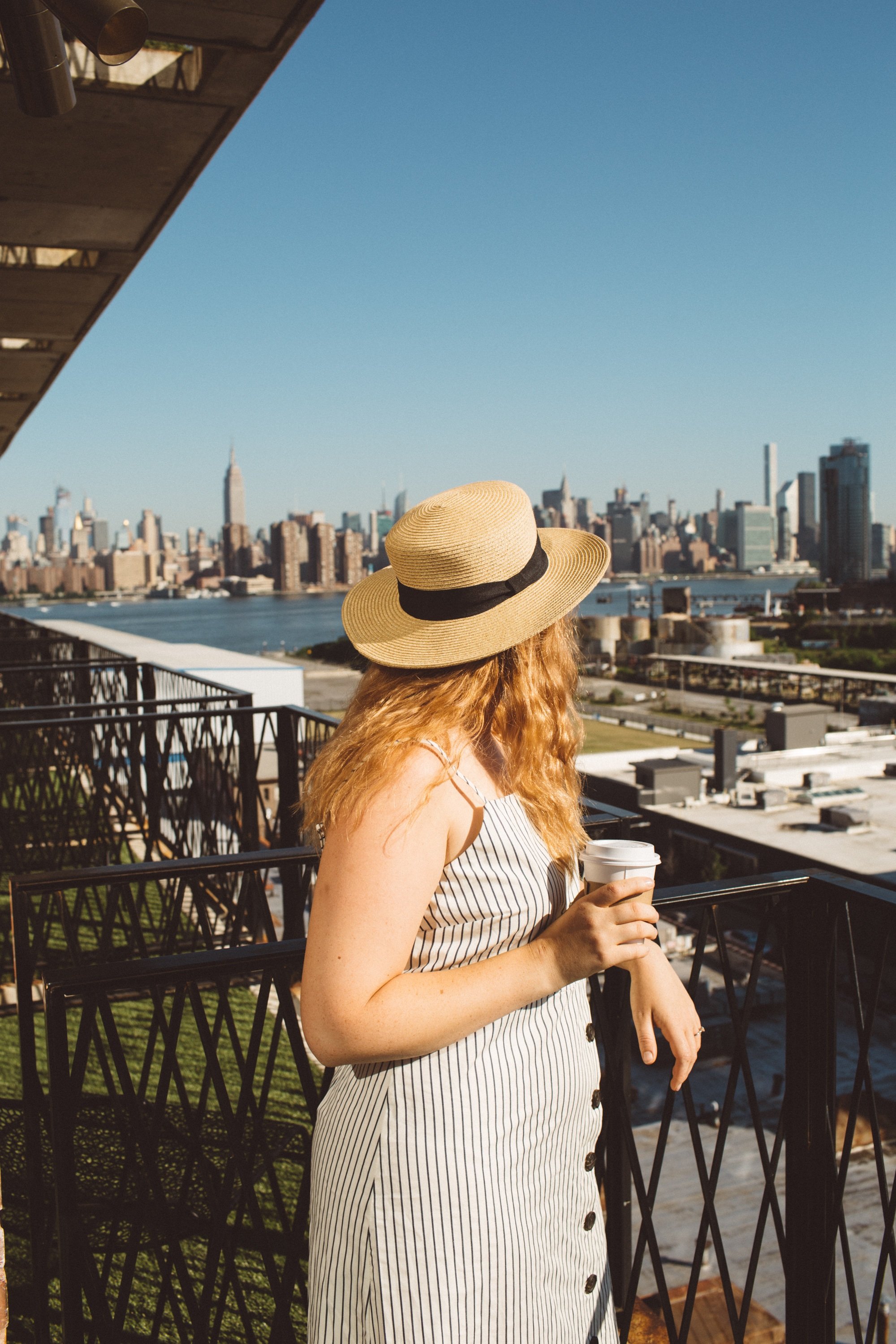 Woman looking at Manhattan from Brooklyn hotel balcony.