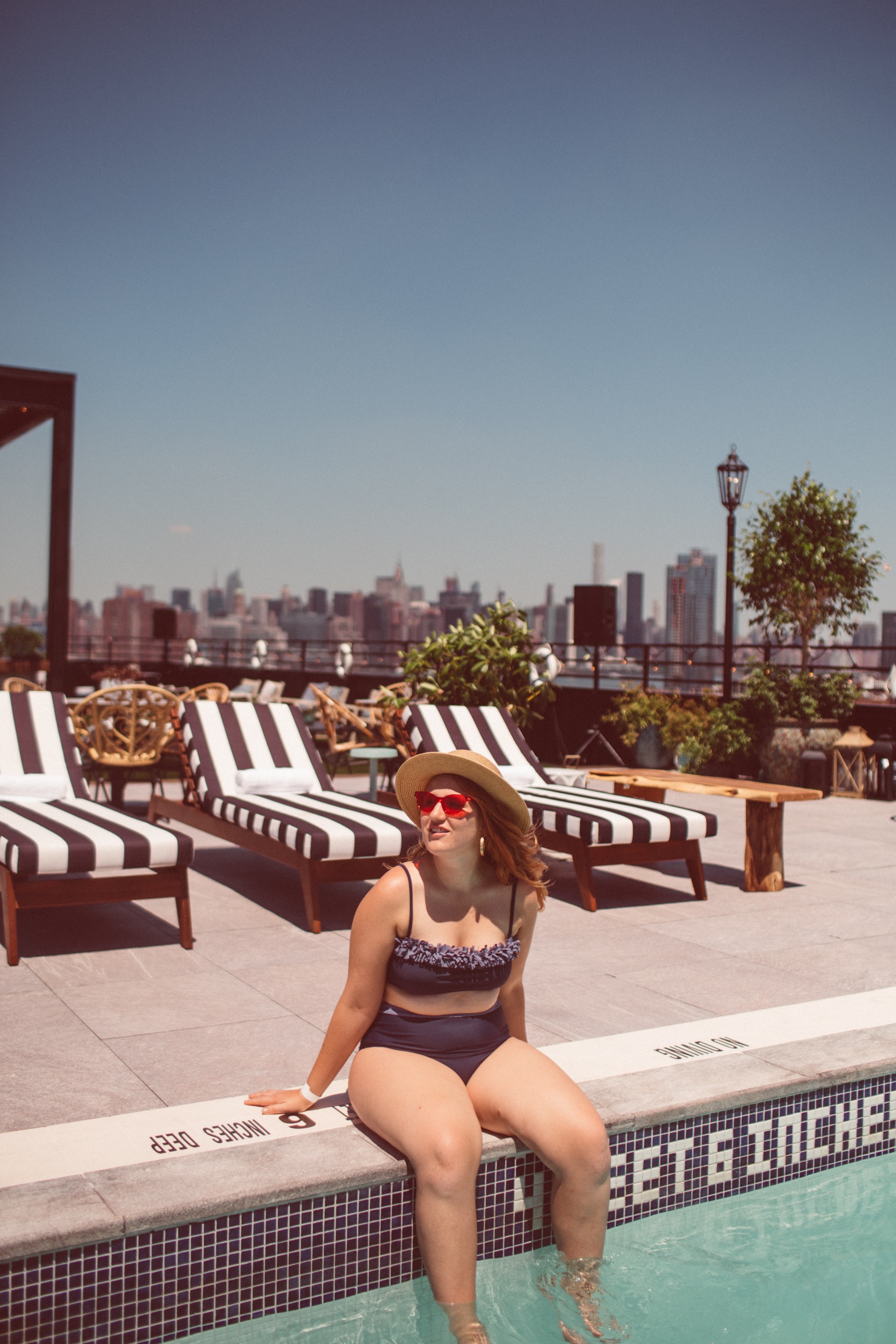 Woman in a swimsuit sitting on the edge of a rooftop pool.