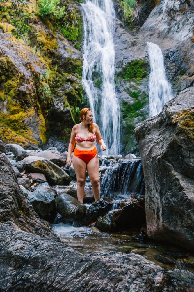 Kara of Whimsy Soul hikes to Feary Falls in Mount Shasta, a stunning small waterfall in Northern California. She is wearing an orange swimsuit