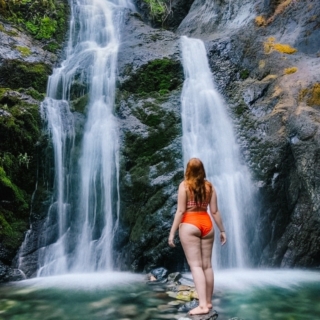 Kara of Whimsy Soul hikes to Feary Falls in Mount Shasta, a stunning small waterfall in Northern California in orange swimsuit