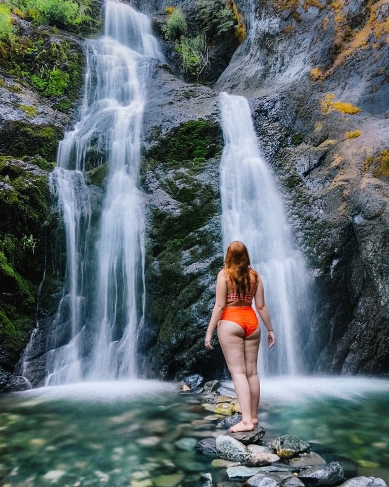 Kara of Whimsy Soul hikes to Feary Falls in Mount Shasta, a stunning small waterfall in Northern California in orange swimsuit